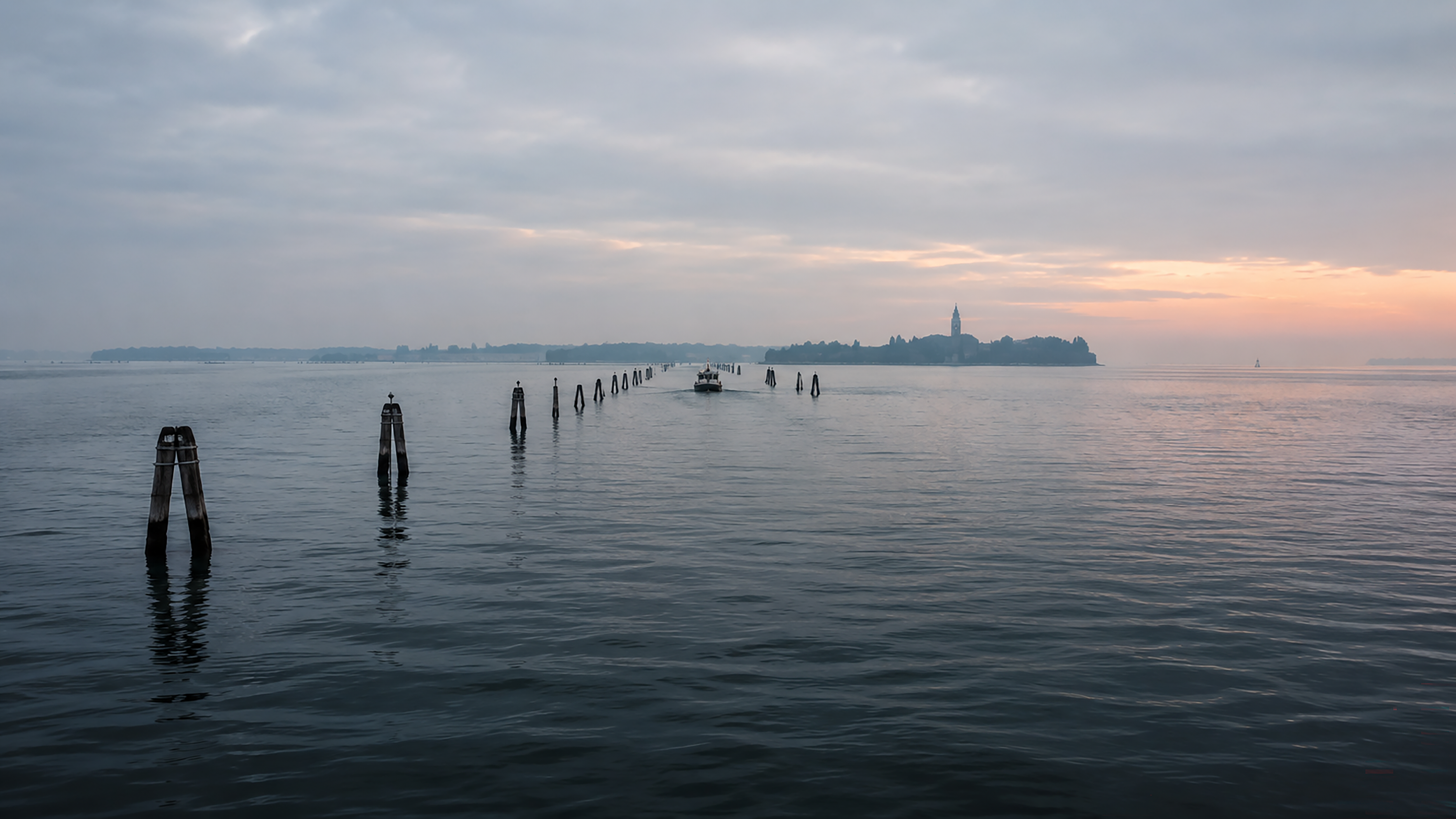 Navigation posts leading across the Venetian Lagoon toward a distant island at dawn