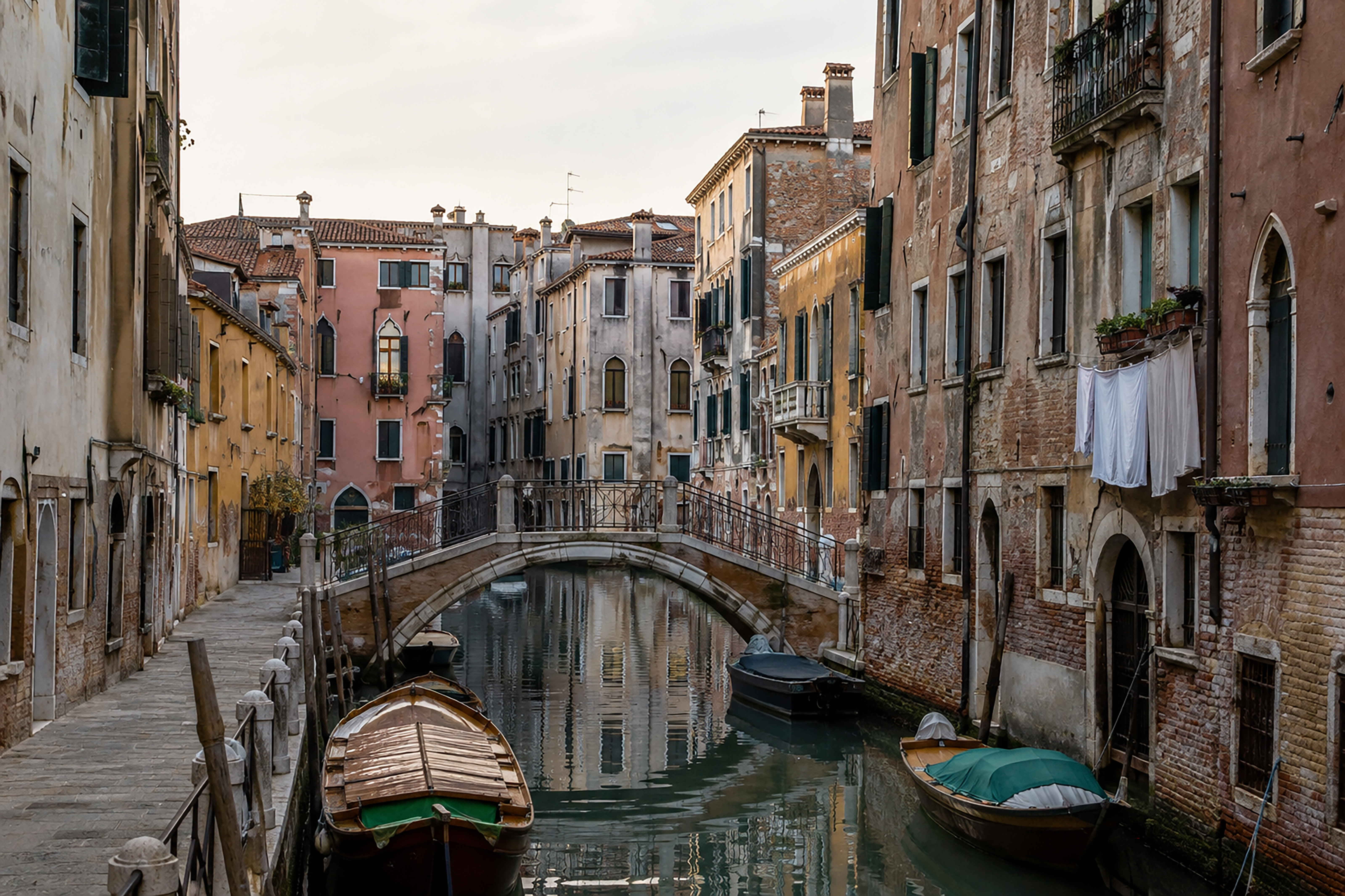 A quiet residential canal with weathered facades, small boats, and a stone footbridge