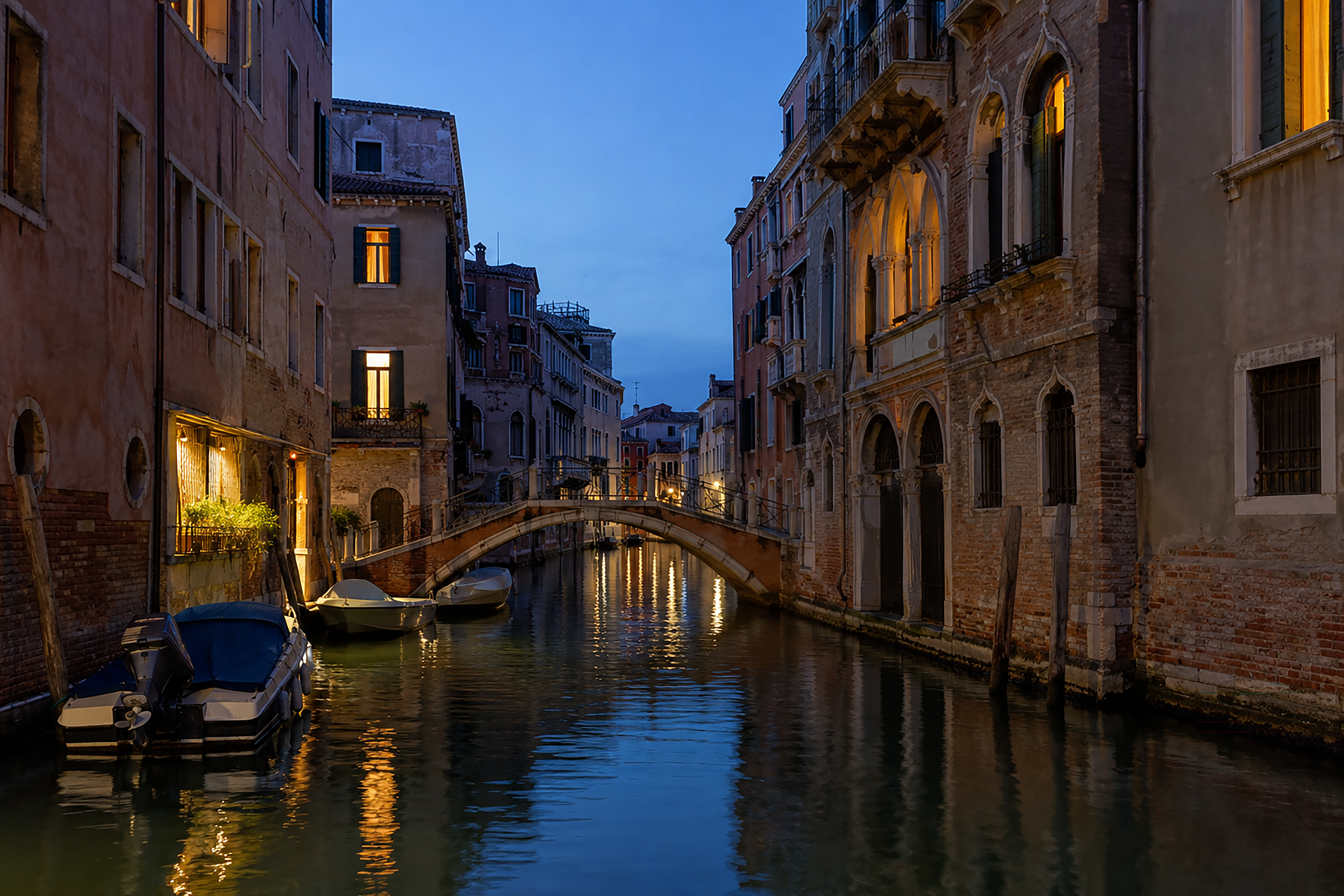 A quiet Venetian canal at blue hour with warm window light reflected on the water